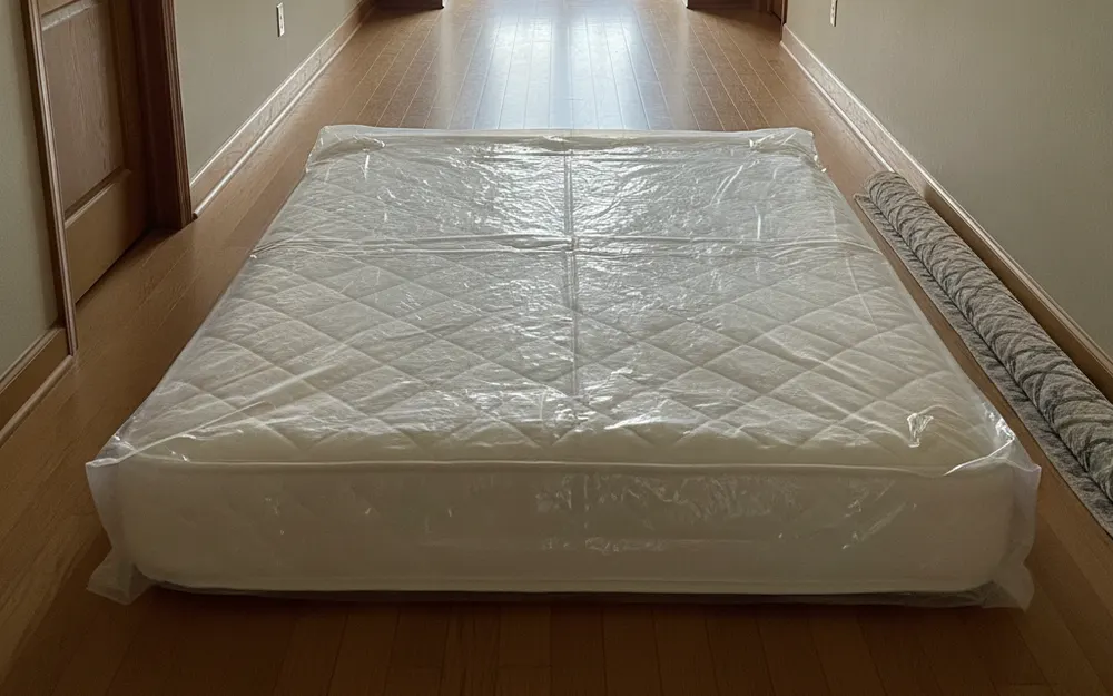 A mattress sealed in a clear plastic bag in a hallway, ready to be carried out